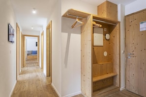 A hallway with wooden flooring, a wooden door with a hanging coat rack, and a view into a room with a bed and a blue wall. - Wi-Fi, 50 meters from downtown, patio, balcony, TV, 72–91 square meters, La Tzoumaz (La Tzoumaz)