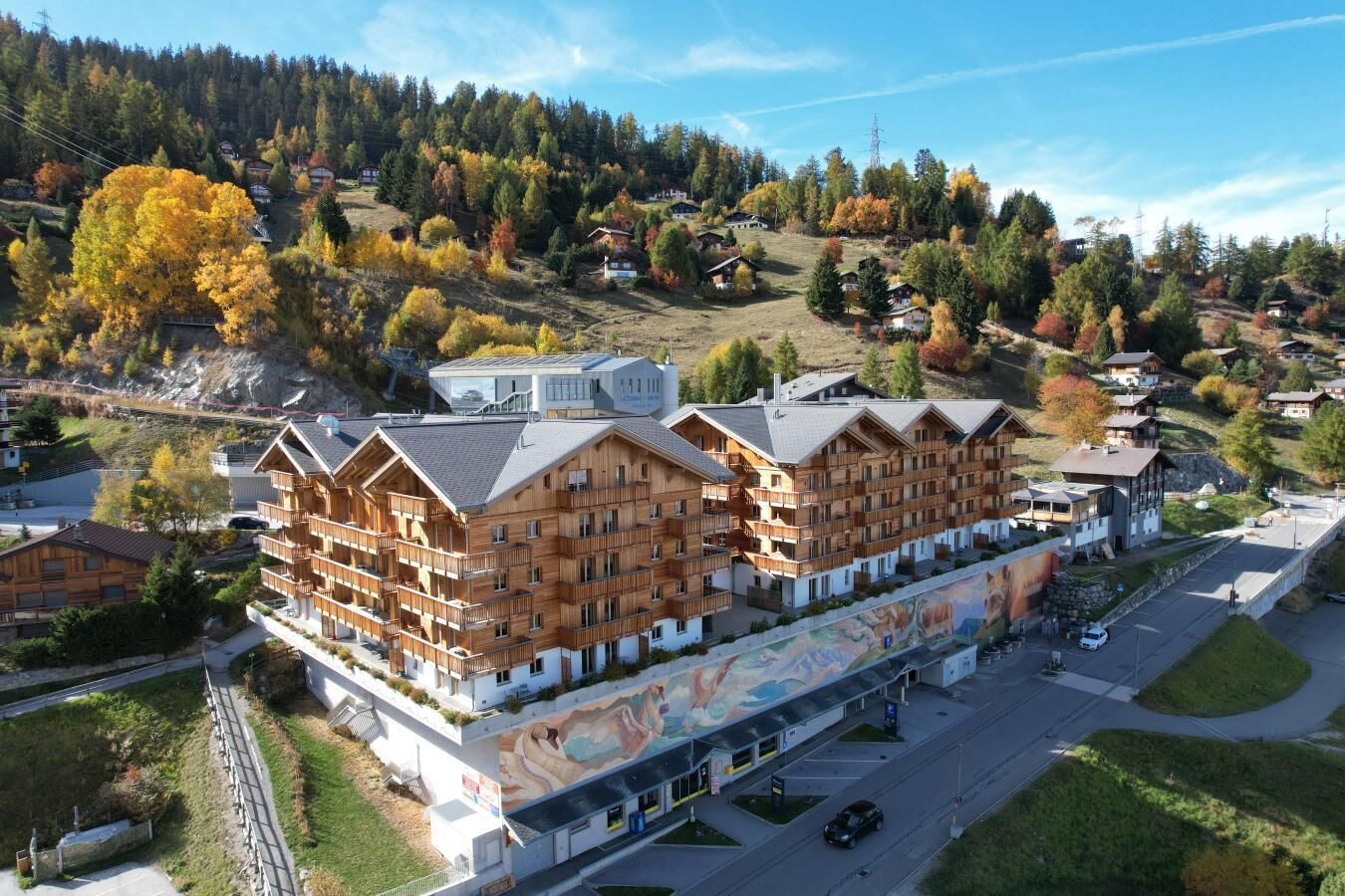 Ein mehrstöckiges Holzgebäude mit Balkonen, einem Wandgemälde und einem Parkplatz.