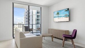 Una sala de estar moderna con un sofá, sillas, una mesa redonda, un televisor y un cuadro con una escena de playa.