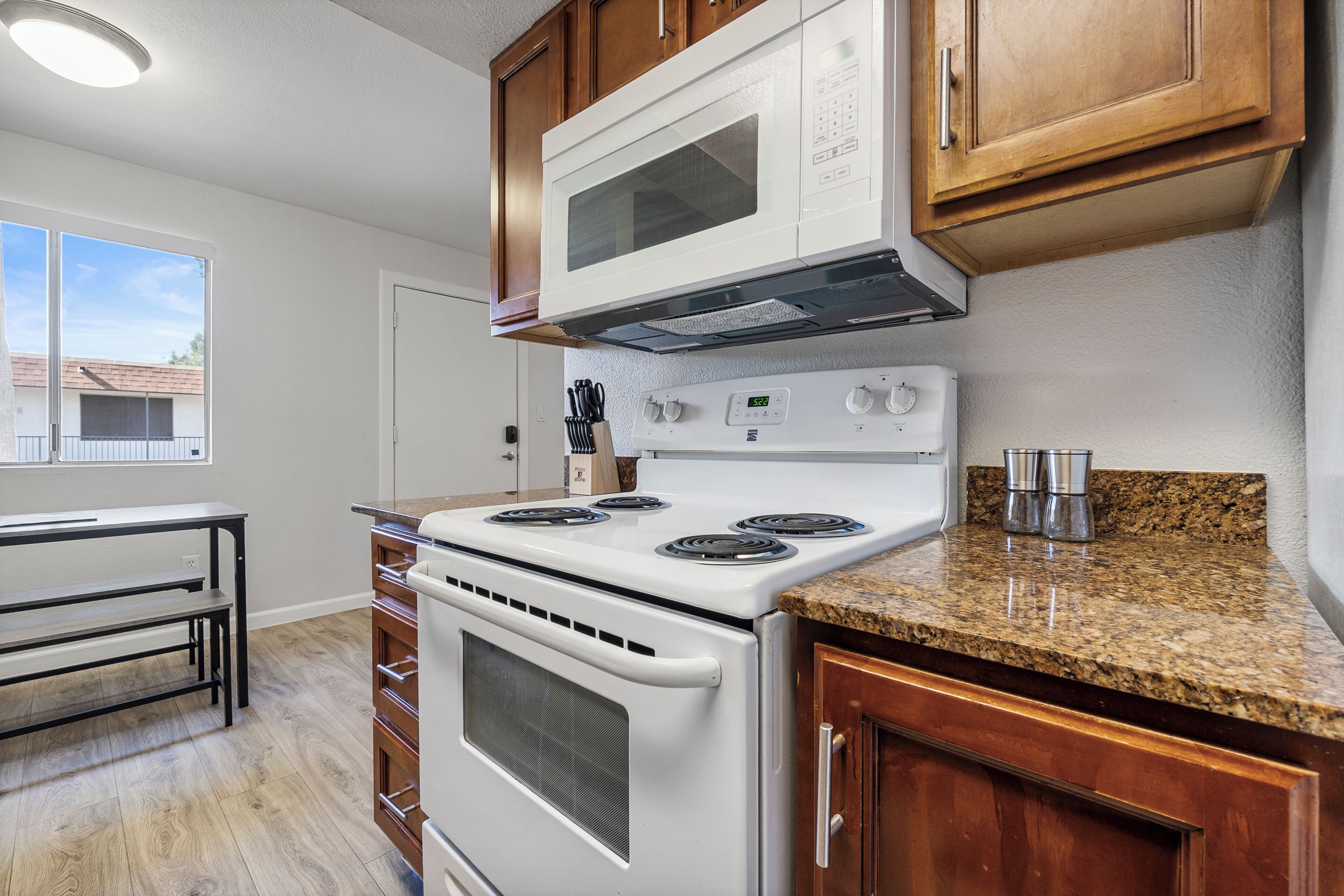 A kitchen with a white stove, microwave, and granite countertop.