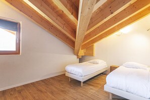 Ein Schlafzimmer mit schrägen Wänden, Holzbalken, zwei Betten und einem Fenster.
