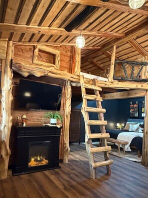 Ein rustikales Blockhaus-Interieur mit Kamin, Holzwänden, einer Leiter und einem Bett.