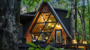Eine moderne Holzhütte mit einer dreieckigen Glasfassade, umgeben von Bäumen.