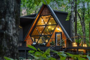 Eine moderne Holzhütte mit einer dreieckigen Glasfassade, umgeben von Bäumen.