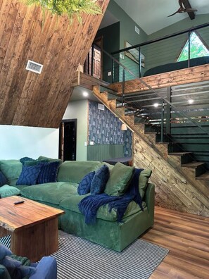 Ein modernes Wohnzimmer mit einem grünen Sofa, einem Holztisch und einer Treppe mit Holzgeländer.