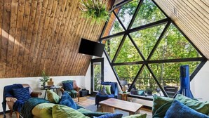 Ein Dachzimmer mit geneigter Decke, großen Fenstern und Blick auf Bäume.