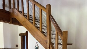Eine Holztreppe mit weißer Brüstung, ein Steinkamin und ein kleiner Tisch mit Korb und Flasche.