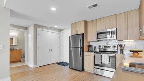 A modern kitchen with stainless steel appliances, wooden cabinets, and a light wood floor.