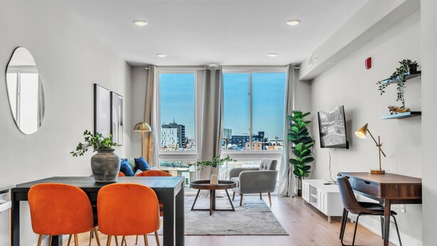 A modern living room with a dining area, large windows, and a city view.