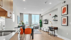 A modern kitchen with a built-in oven, a dining area with a table and chairs, and a living space with a TV and artwork on the wall.