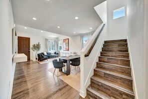 Un intérieur moderne comprenant un escalier, un plancher en bois, un coin repas avec une table et des chaises, et un salon avec un canapé et une plante.