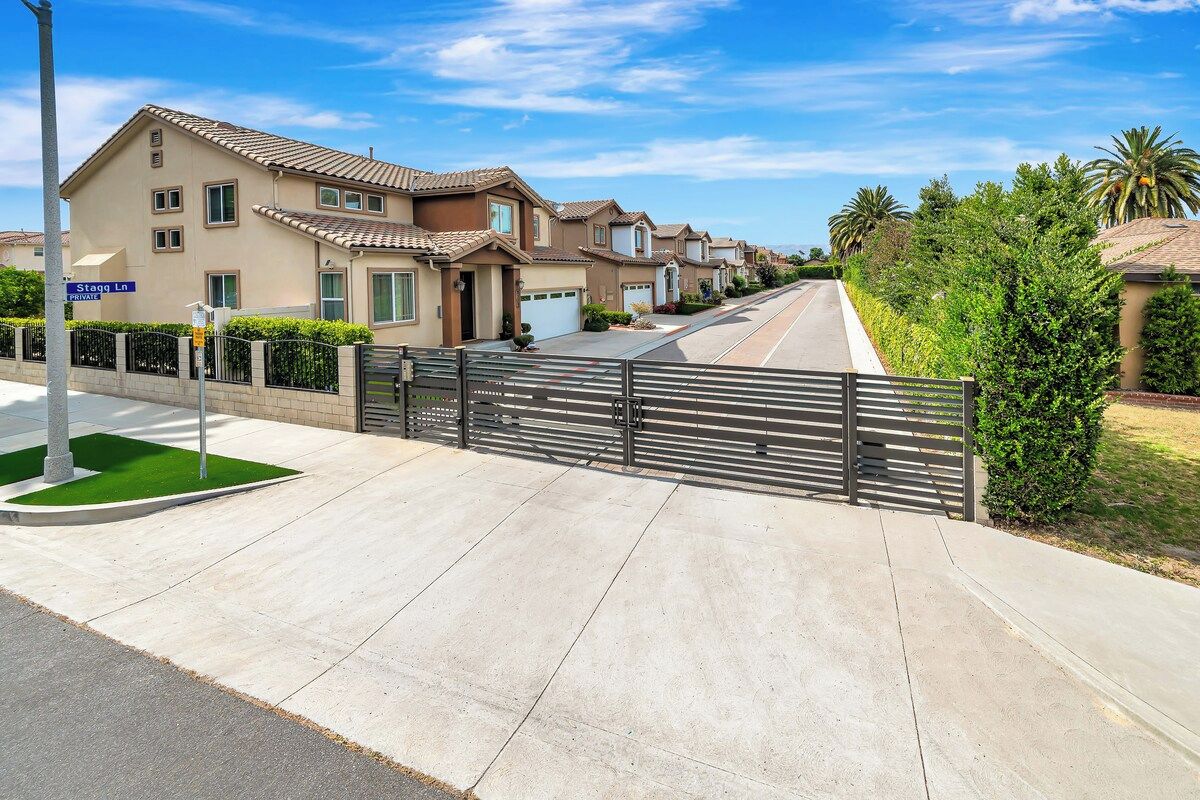 Une rue résidentielle bordée de maisons, avec une allée privée fermée par un portail et un ciel dégagé.