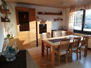 Ruokailutila, jossa on puinen pöytä ja tuolit, sisäänrakennettu uuni ja ikkuna, jossa on verhot.