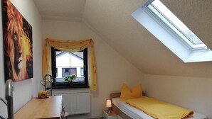 Ein Schlafzimmer mit Dachfenster, einem Bett mit gelber Bettwäsche, einem Schreibtisch und einem Heizkörper.