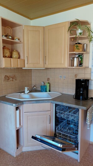 A compact kitchen with a built-in dishwasher, a coffee maker, and a potted plant.