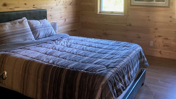 Un dormitorio con una cama, paredes de madera, una ventana y un cuadro en la pared.