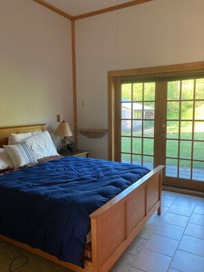 Ein Schlafzimmer mit einem Holzbett, einem Nachttisch, einer Lampe und Blick auf eine grüne Landschaft durch eine Glastür.