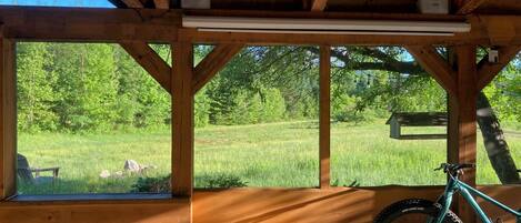 A covered outdoor area with a wooden bench, a bicycle, and a view of a grassy field.