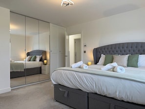 Ein Schlafzimmer mit einem großen Bett, einem Kleiderschrank mit Spiegel und einem Nachttisch mit Lampe.