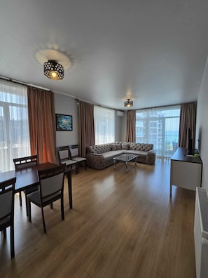 Ein modernes Wohnzimmer mit Ecksofa, Esstisch, Stühlen und einem Fernseher.