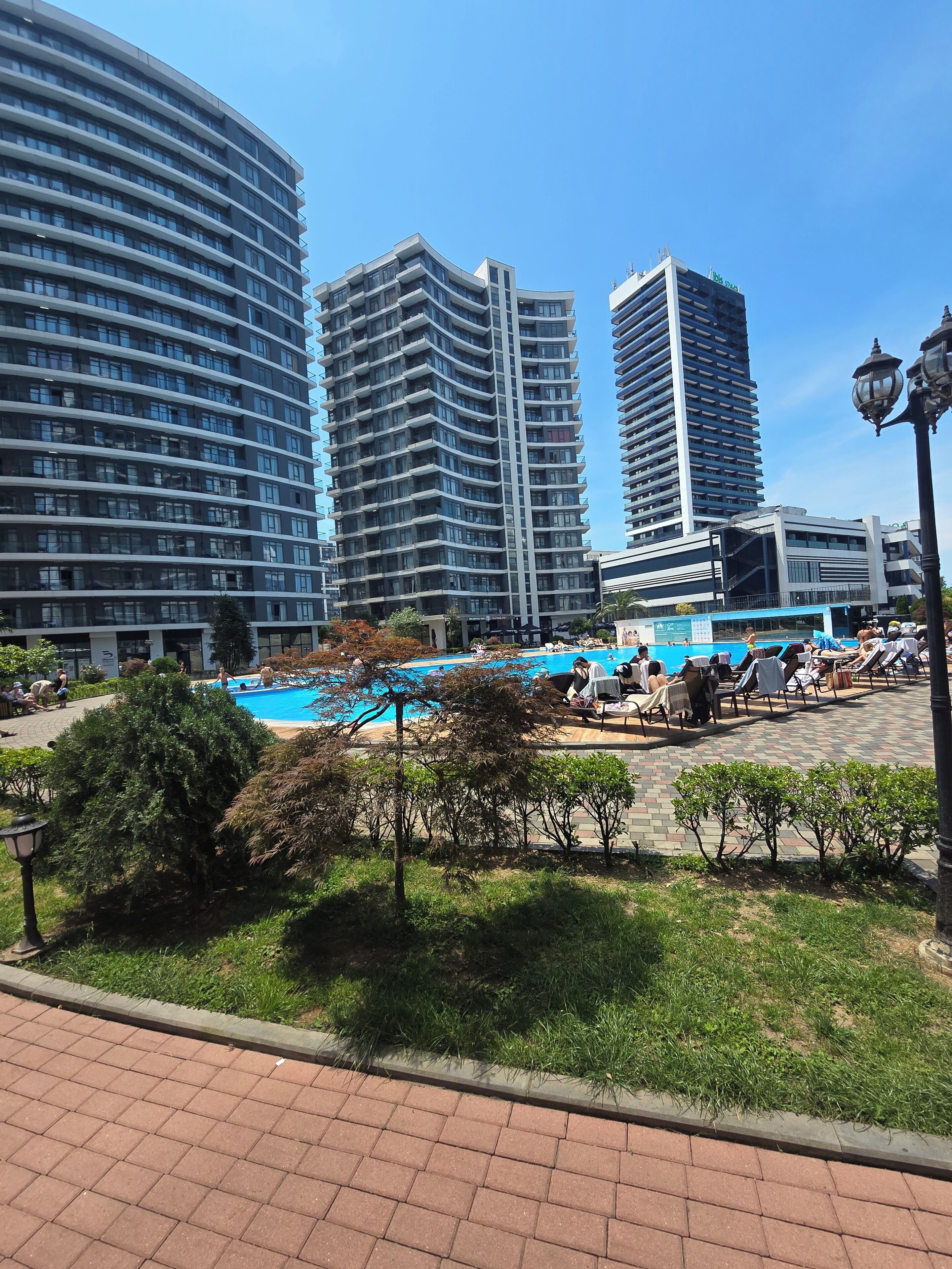 Ein modernes Hotel mit Schwimmbad, umgeben von Grünflächen und Hochhäusern.