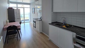 Una cocina moderna con armarios blancos, encimera negra y un lavamanos. Hay un comedor con una mesa y sillas.