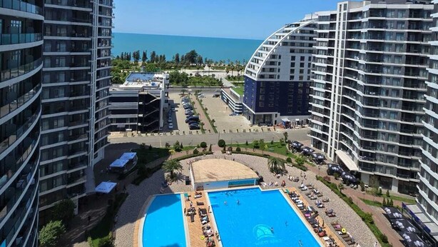 Un hotel de gran altura con una piscina central, varios balcones y vistas al mar.