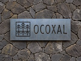 Un letrero de metal con la palabra 'OCOXAL' y un símbolo de árboles.