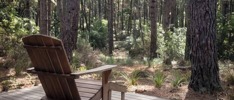 Una terraza de madera con una sola silla Adirondack mirando hacia un bosque.