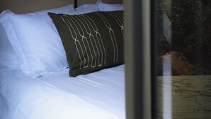 Un lit avec une literie blanche et un oreiller foncé orné d’un motif blanc.