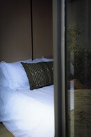 Una cama con ropa de cama blanca y un almohadón oscuro con diseño blanco.