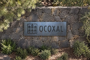 Un muro de piedra con un letrero de metal que dice 'OCOXAL' y un símbolo de árboles.