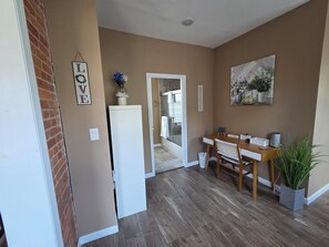 A hallway with a white refrigerator, a dining table with chairs, a potted plant, and a framed picture on the wall. - Cozy 1-bedroom Queen City Urban Escape (Cincinnati)