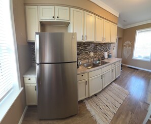 A kitchen with a stainless steel refrigerator, white cabinets, a tiled backsplash, and a wooden floor. - Cozy 1-bedroom Queen City Urban Escape (Cincinnati)