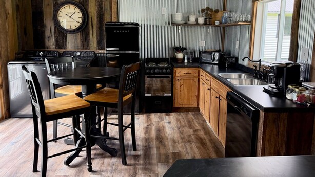 A kitchen with a wooden table, chairs, a clock, a refrigerator, a stove, a microwave, and a sink. - Cumberland Blue- Cozy, Rustic Cottage Near Lake Cumberland (Jamestown)