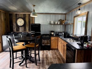 A kitchen with a wooden table, chairs, a clock, a refrigerator, a stove, a microwave, and a sink.