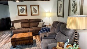 A living room with a brown sofa, a wooden coffee table, a lamp, and framed equestrian artwork on the wall. - Cumberland Blue- Cozy, Rustic Cottage Near Lake Cumberland (Jamestown)