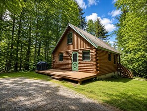 Une cabane en rondins dotée d’une véranda, d’un barbecue couvert et d’un escalier menant à l’entrée.