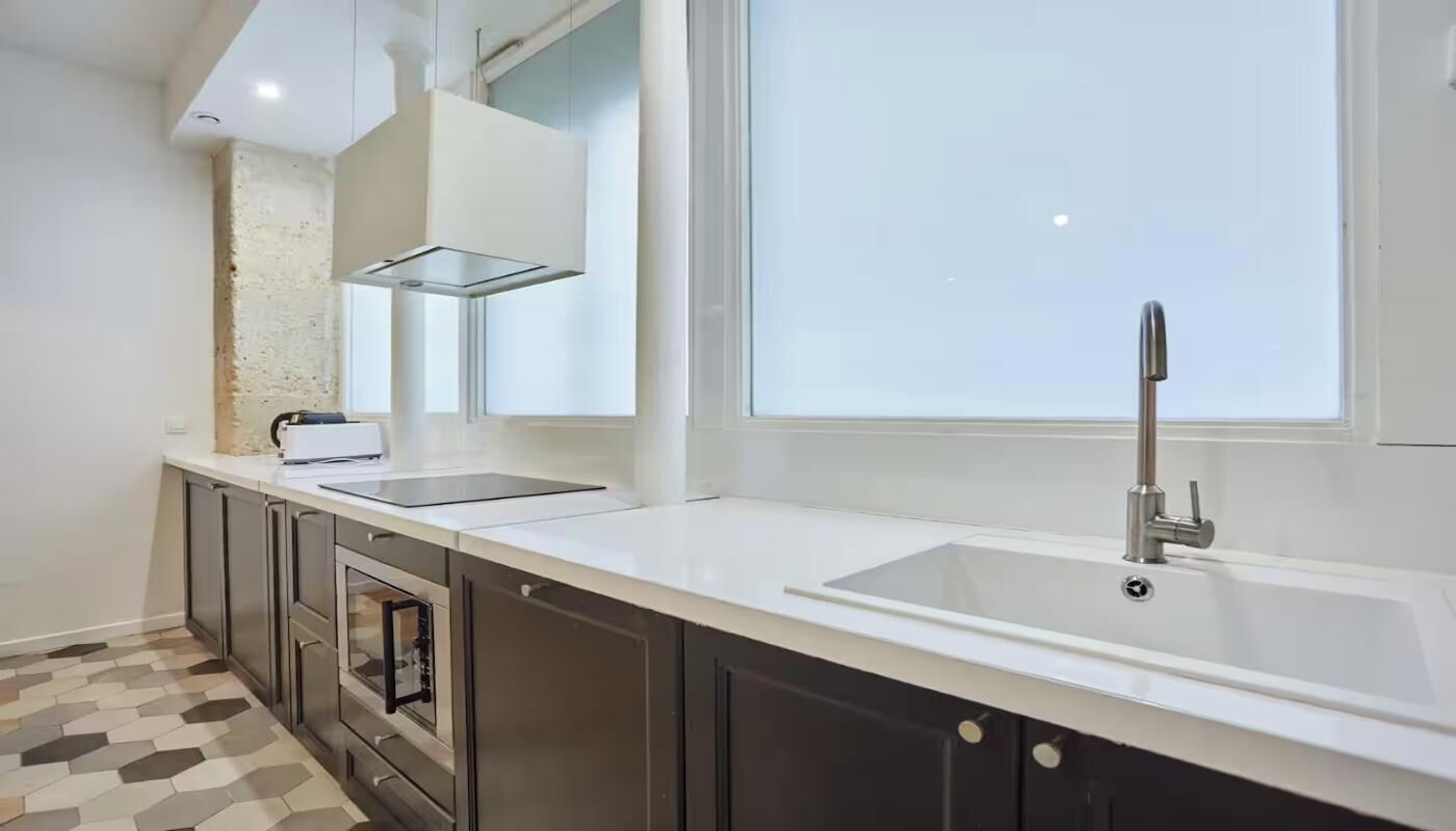 A modern kitchen with a large window, a built-in oven, and a stainless steel sink.