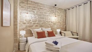 Een hotelkamer met een stenen muur, een bed met wit beddengoed, twee bedlampjes en een stoel.