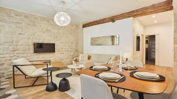 Een eetgedeelte met een houten tafel voor vier personen, een stenen muur, een tv aan de wand en een moderne hanglamp.