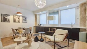 Een moderne keuken met donkere kastjes, een groot raam en een eethoek met een ronde tafel en stoelen.
