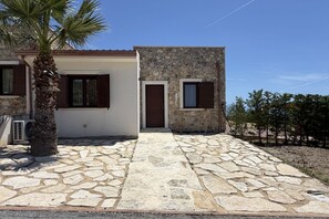 Un chemin de pierres menant à une maison avec un palmier, des murs en pierre et une porte.