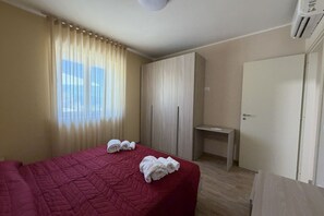 A hotel room with a bed, a desk, a wardrobe, and a window with curtains. - Sea-view apartment with a pool (Telegrafo)