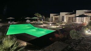 A nighttime view of a swimming pool area with lounge chairs and umbrellas, surrounded by landscaped gardens and modern buildings. - Sea-view apartment with a pool (Telegrafo)