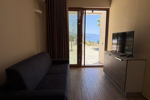 Ein Zimmer mit einer Couch, einem Fernseher auf einer Kommode und einer Glastür zum Balkon mit Blick.