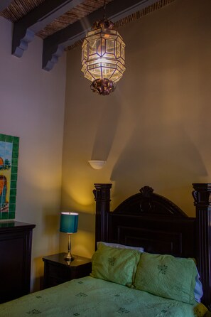 A bedroom with a bed, a nightstand, a lamp, and a hanging light fixture.