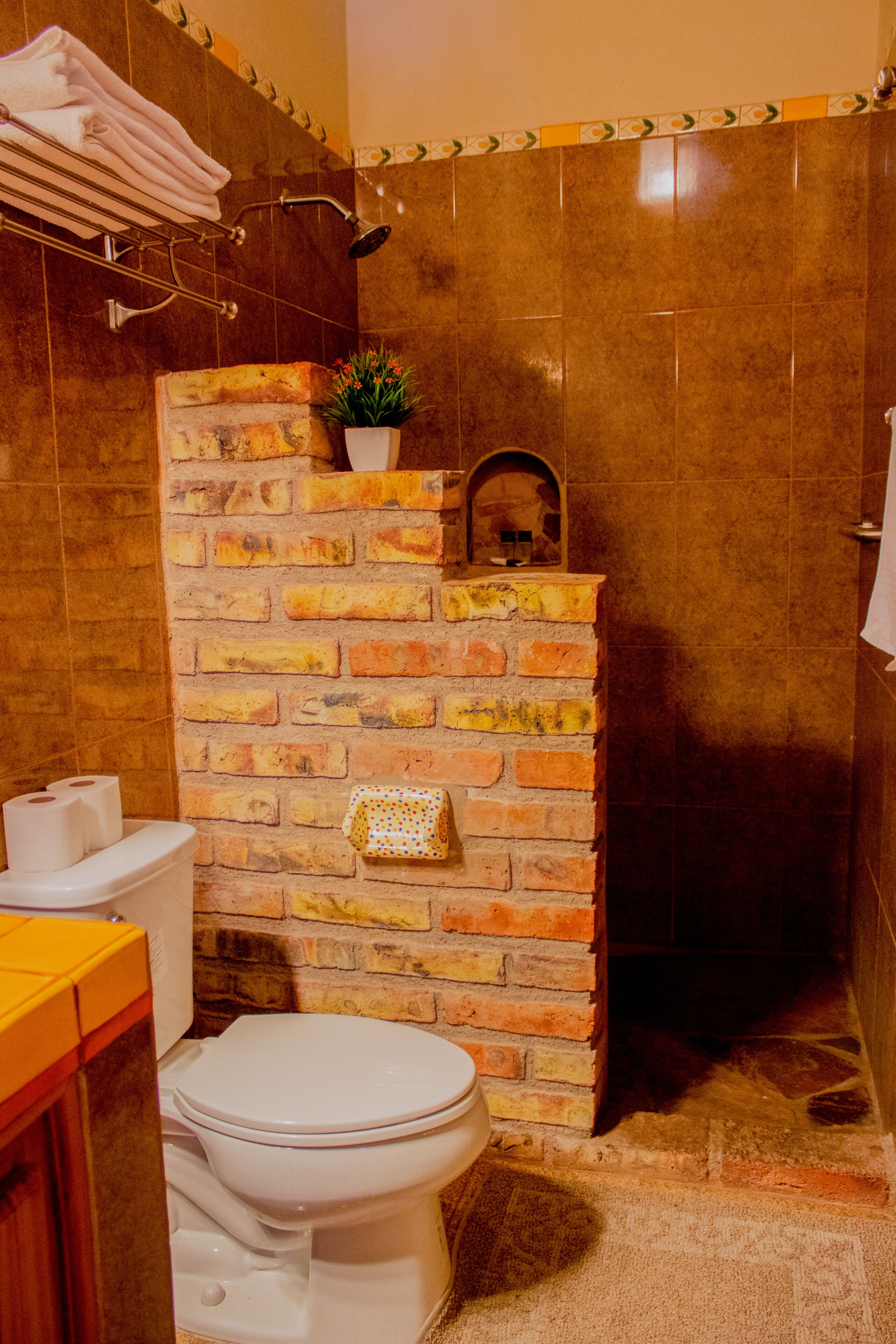 Un baño con pared de ladrillo, inodoro blanco, lavamanos y zona de ducha.