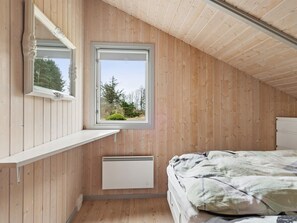 Ein Zimmer mit Holzwänden, einem Fenster mit Blick auf Bäume, einem Bett und einem weißen Heizkörper.