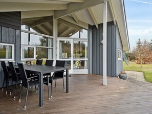 Ein überdachter Außenbereich mit Tisch und Stühlen, großen Fenstern und Blick auf die umliegende Landschaft.